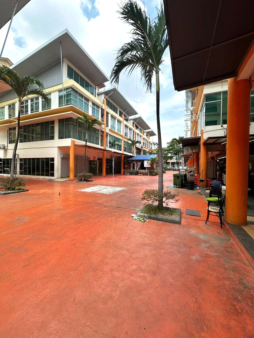 Exterior type: shophouse; features: orange painted concrete flooring, palm trees, multiple-storey buildings, glass windows, overhangs, outdoor seating area, manicured landscaping, commercial spaces, covered walkways, open courtyard; style: modern.